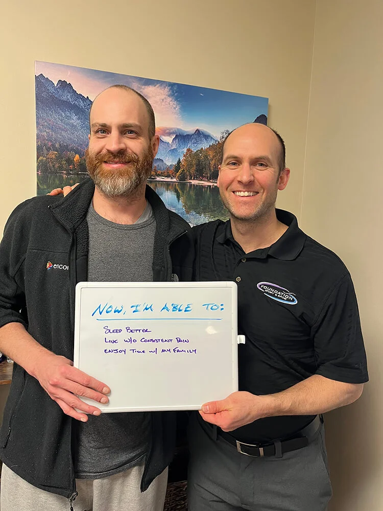 Dr. Nate Porcher, chiropractor Arlington Heights, posing with a patient in his clinic holding a sign